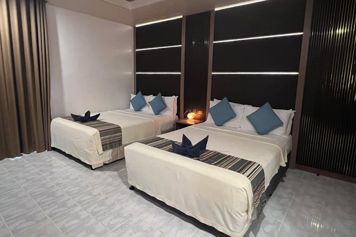 A hotel room with two beds, a nightstand, and a wall-mounted light fixture.