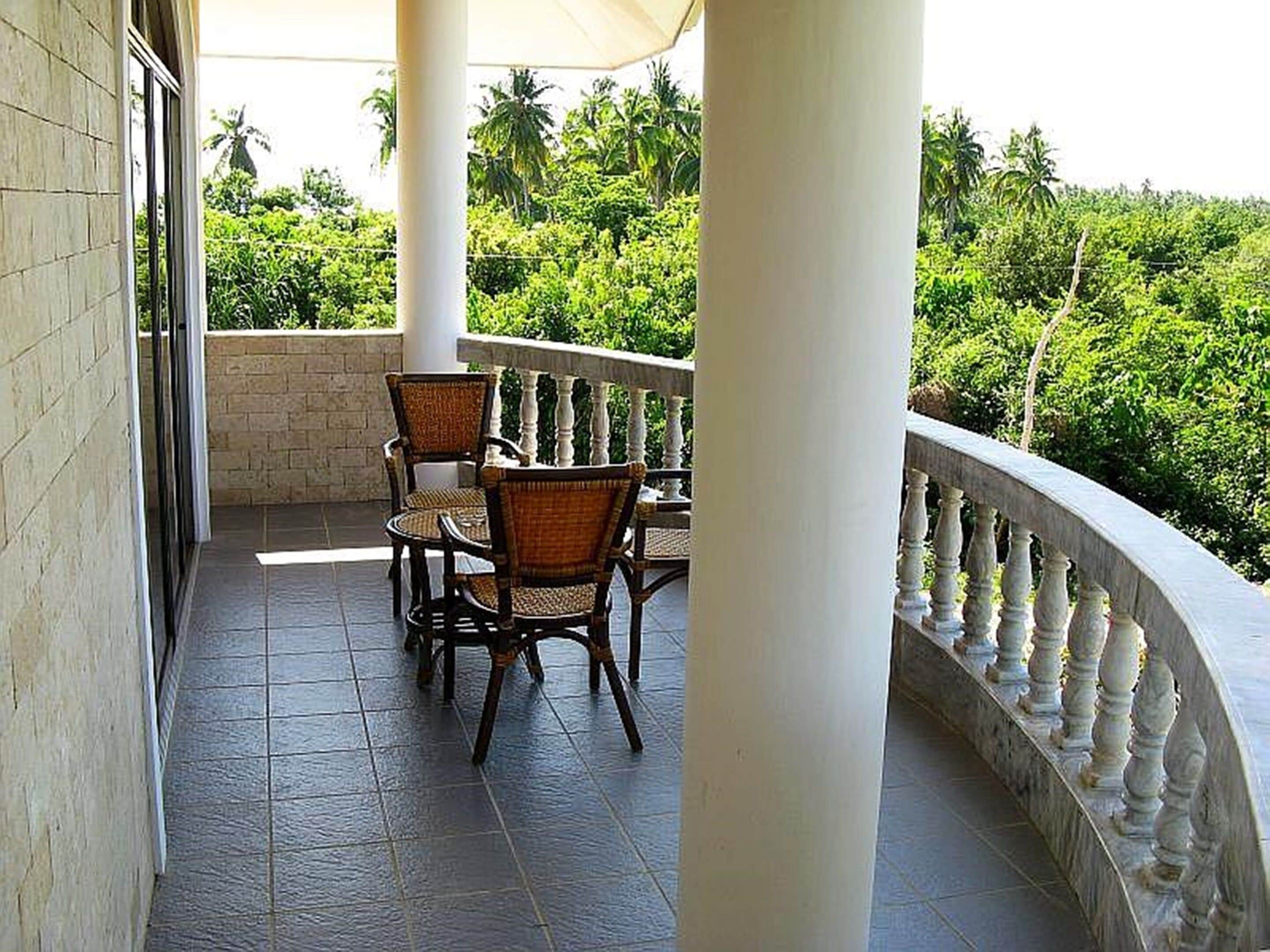 Ein Balkon mit Tisch und Stühlen, umgeben von einer weißen Balustrade, mit Blick auf eine üppige grüne Landschaft.