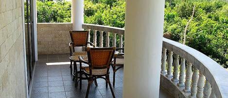 Ein Balkon mit Tisch und Stühlen, umgeben von einer weißen Balustrade, mit Blick auf eine üppige grüne Landschaft.