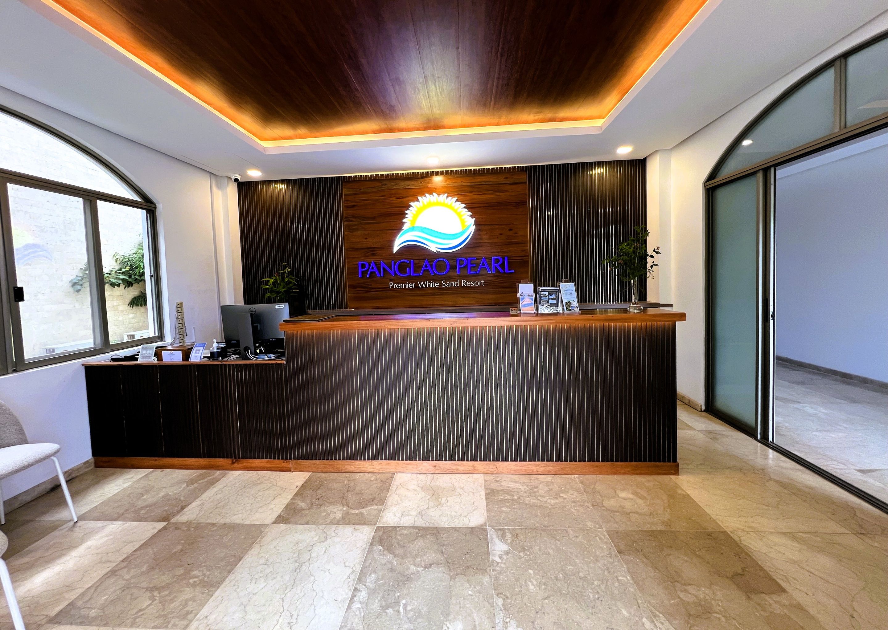 A reception desk with a wooden finish, a logo, and a nameplate for 'Panglao Pearl Premier White Sand Resort.'