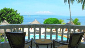 Un balcon avec des fauteuils en osier et une petite table, donnant sur une piscine et la mer.