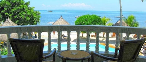 Un balcon avec des fauteuils en osier et une petite table, donnant sur une piscine et la mer.