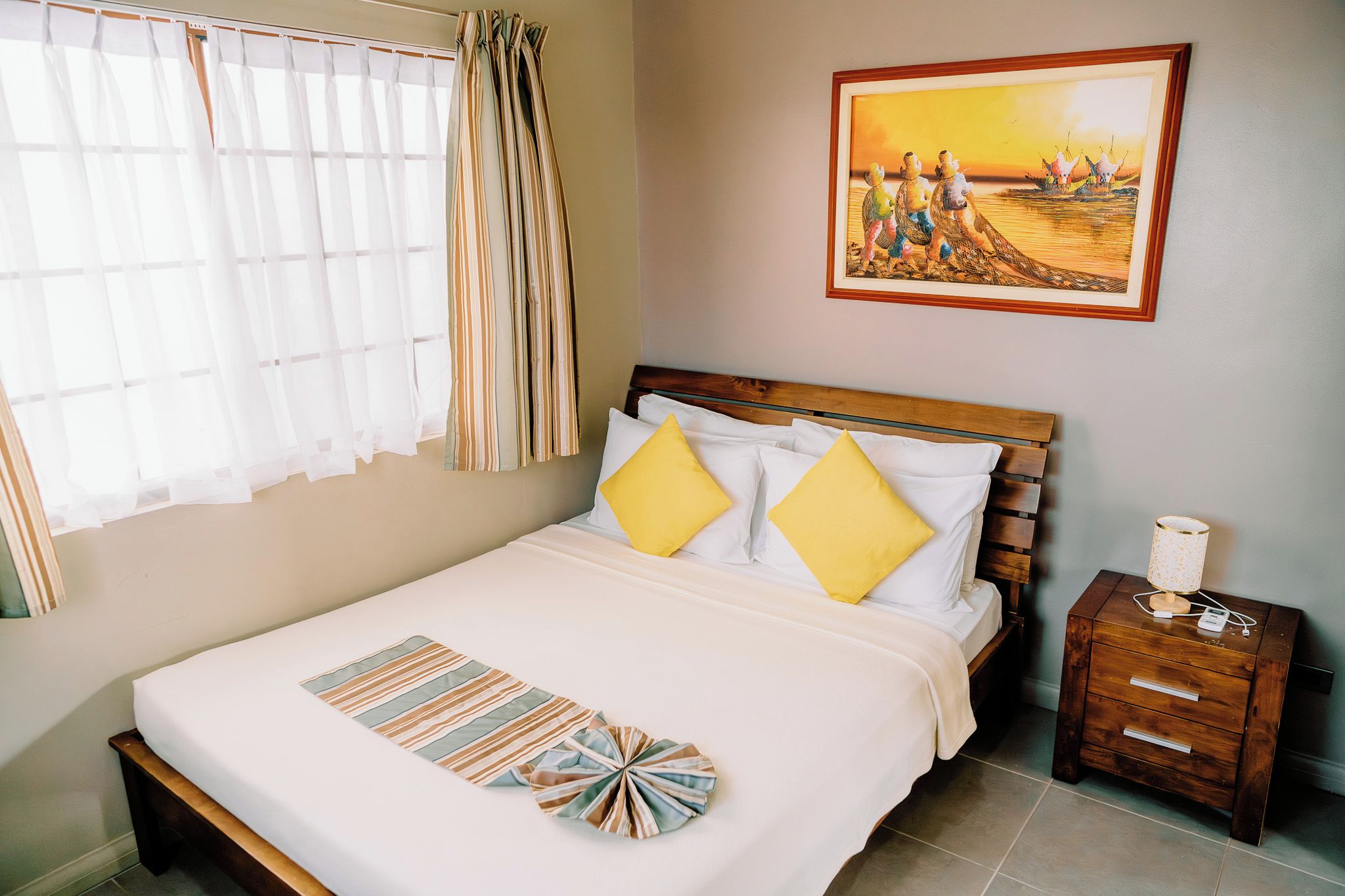 A neatly made bed with two pillows, a bedside table with a lamp, and a painting on the wall.