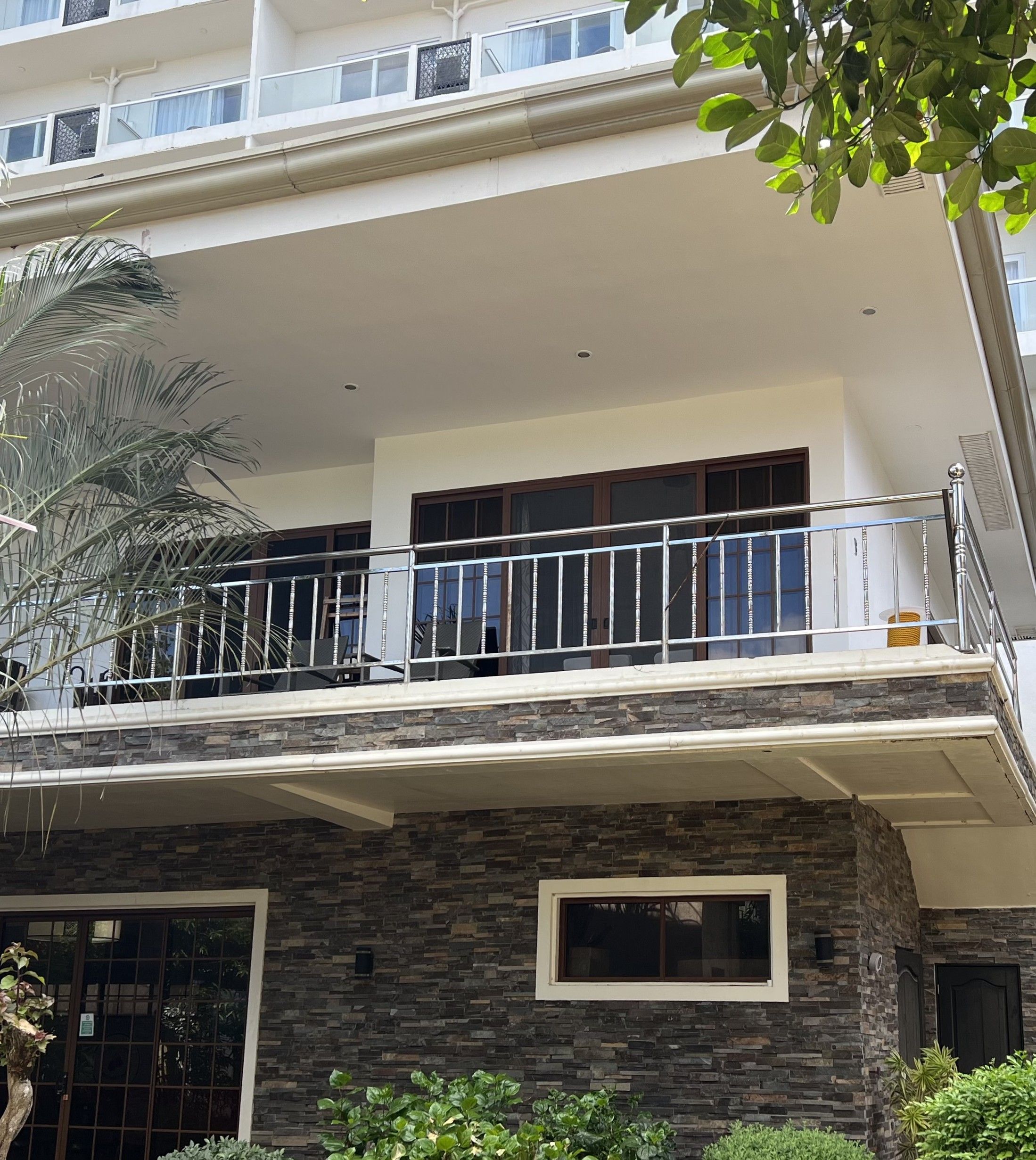 A multi-story residential building with a balcony, stone facade, and a window with a view.