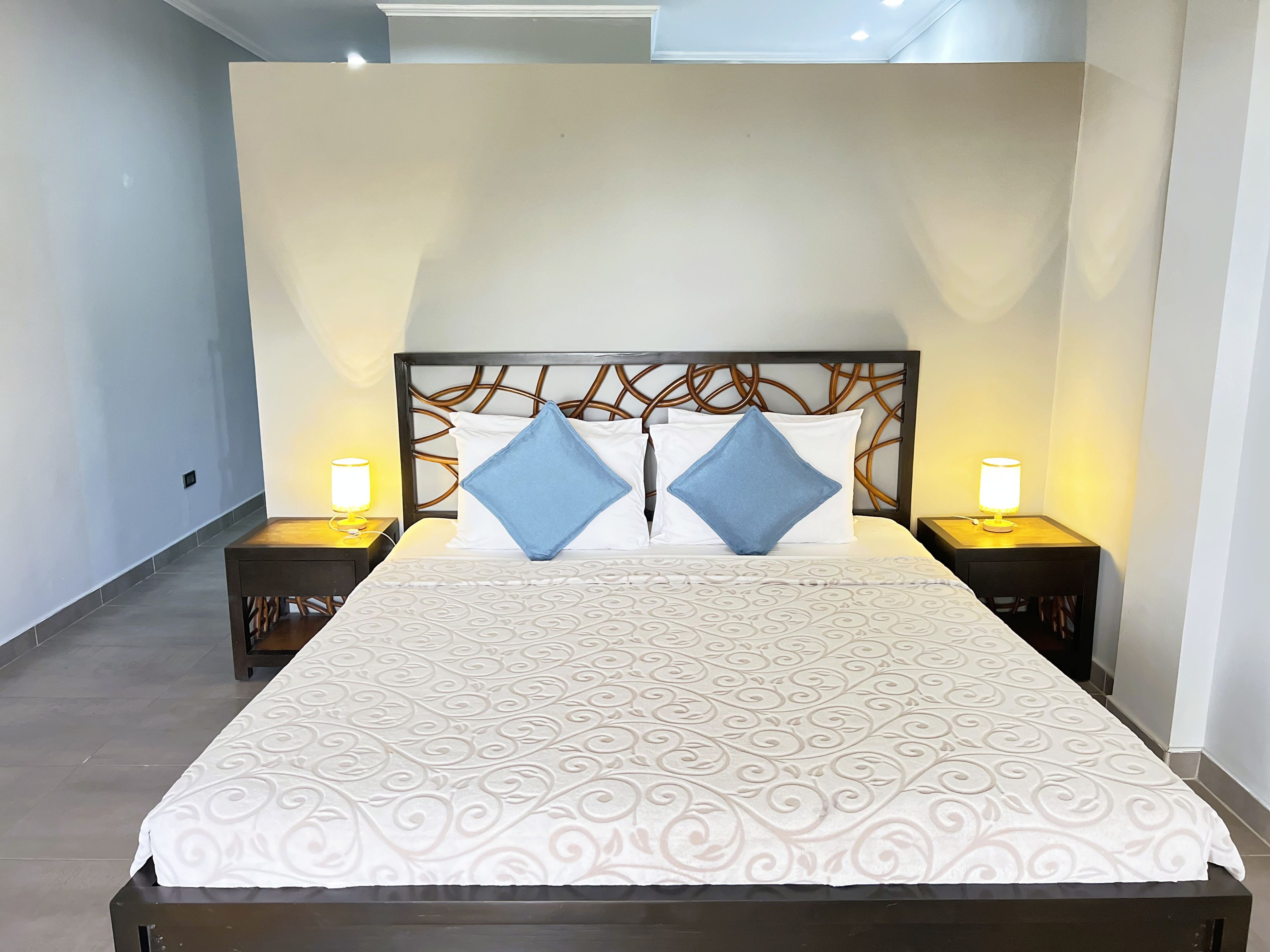 Una cama bien hecha con una colcha estampada, dos almohadas y dos lámparas de noche.