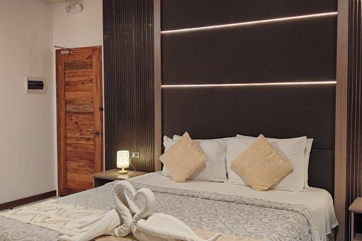 A modern bedroom with a large bed, a wooden door, and a nightstand with a lamp.