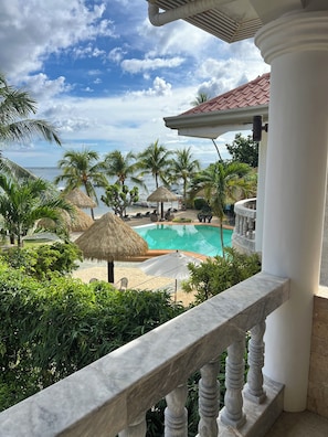 A pool area with a view of the ocean, surrounded by palm trees and thatched umbrellas. - Panglao Pearl Premier White Sand Resort (Panglao)