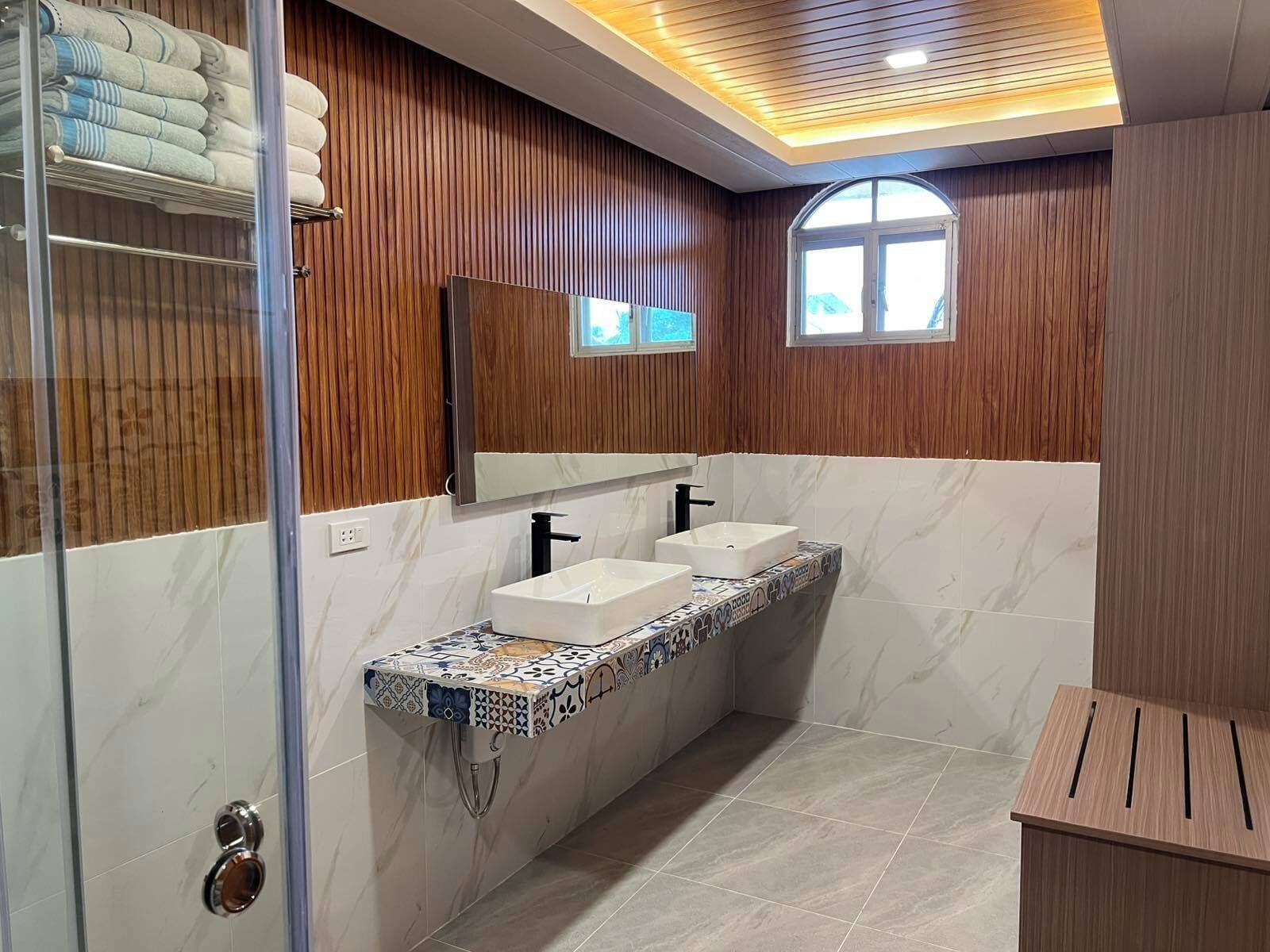 Ein modernes Badezimmer mit Holzvertäfelung, einem großen Spiegel, zwei Waschbecken und einer Duschkabine.