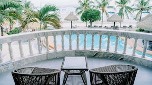 Un espace aménagé au bord de la piscine, avec une balustrade en marbre, des fauteuils en osier et une vue sur la plage.
