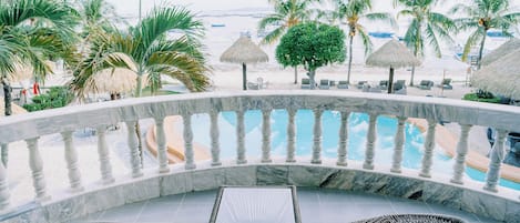 Zona junto a la piscina con barandilla de mármol, sillas de mimbre y vista a la playa.