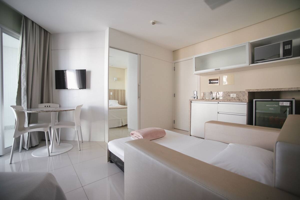 A hotel room with a bed, a desk, a chair, a television, a kitchenette, and a bathroom.