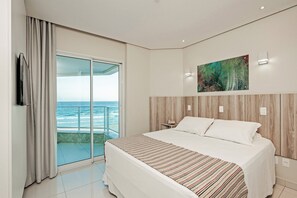 A hotel room with a large bed, a painting on the wall, and a view of the ocean through a sliding glass door. - SLAVIERO  Ingleses Convention (Florianópolis)