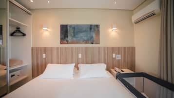 A hotel room with a bed, bedside tables, a hanging coat rack, and a painting on the wall.