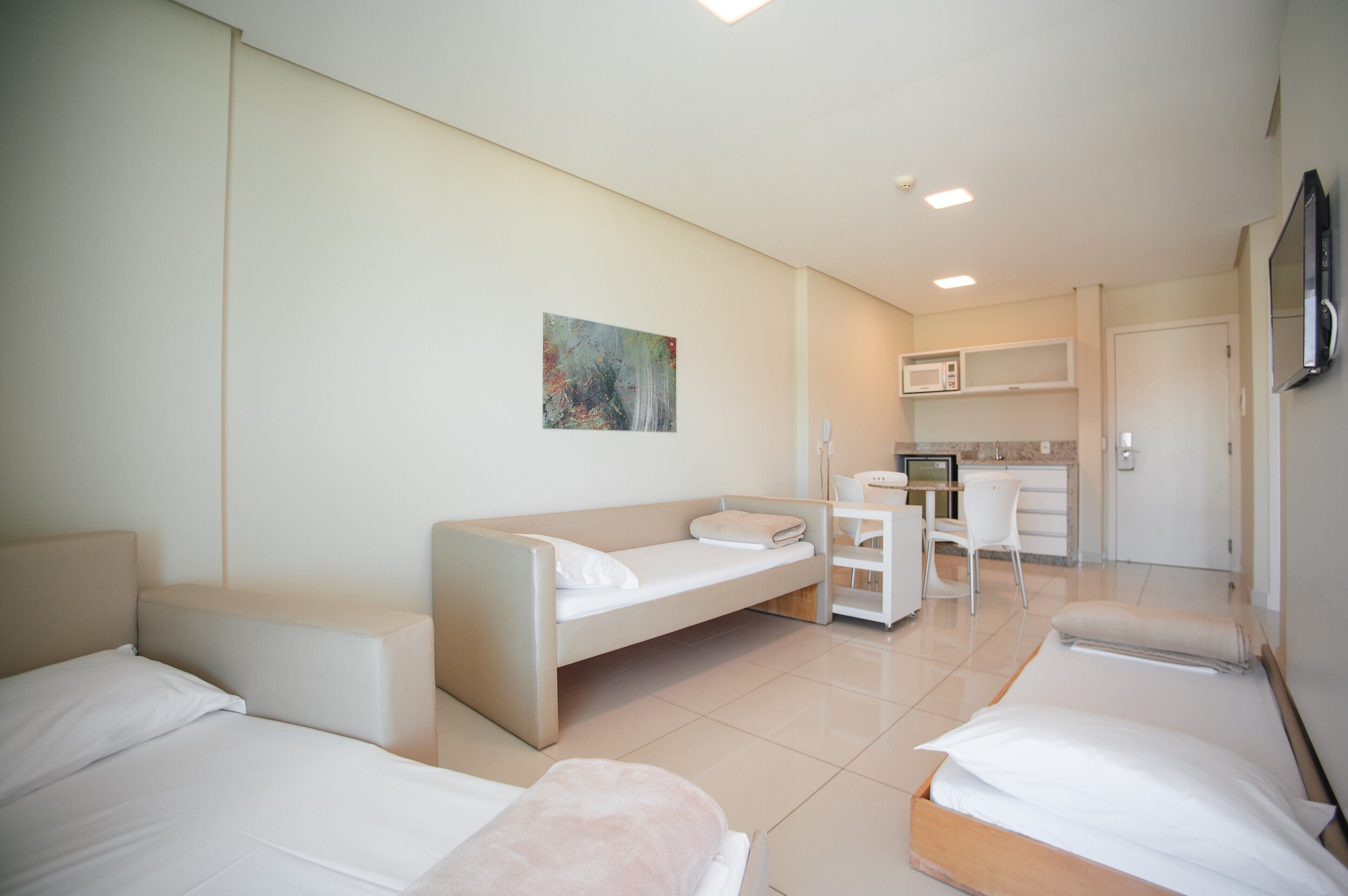 Ein Hotelzimmer mit zwei Betten, einer Couch, einer kleinen Küchenzeile und einem Fernseher.