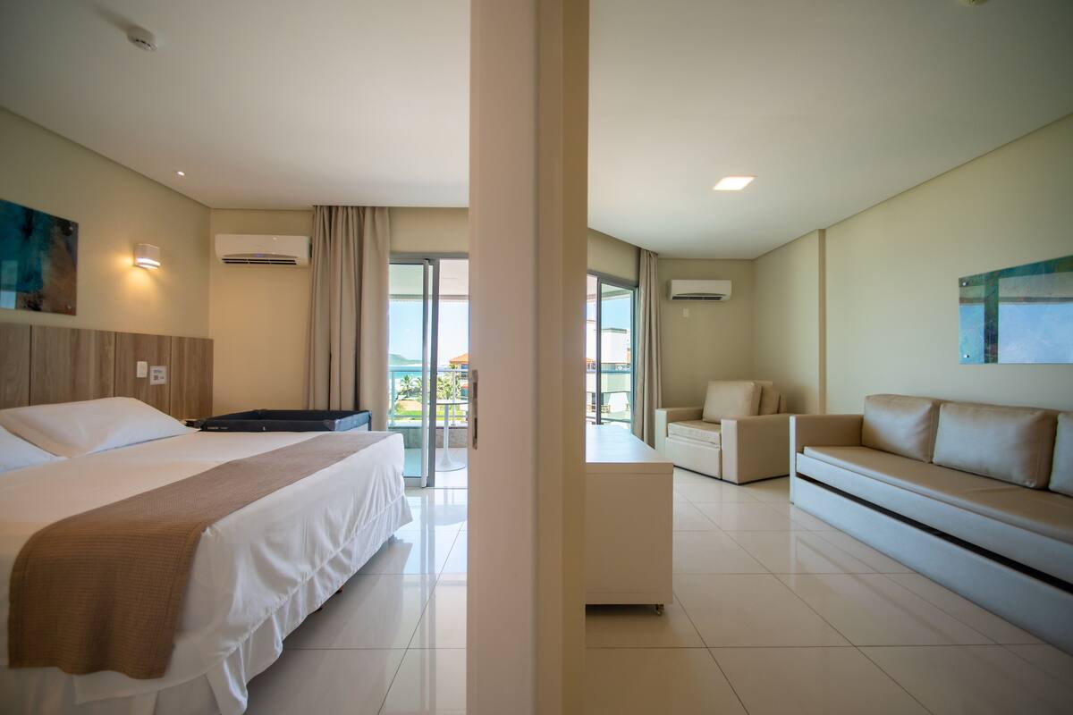 A hotel room with a bed, a sofa, a desk, and a balcony with a view.