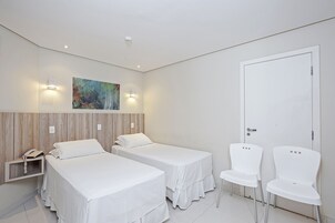 Camera d'albergo con due letti singoli, una testiera in legno, un quadro appeso e una porta con maniglia.