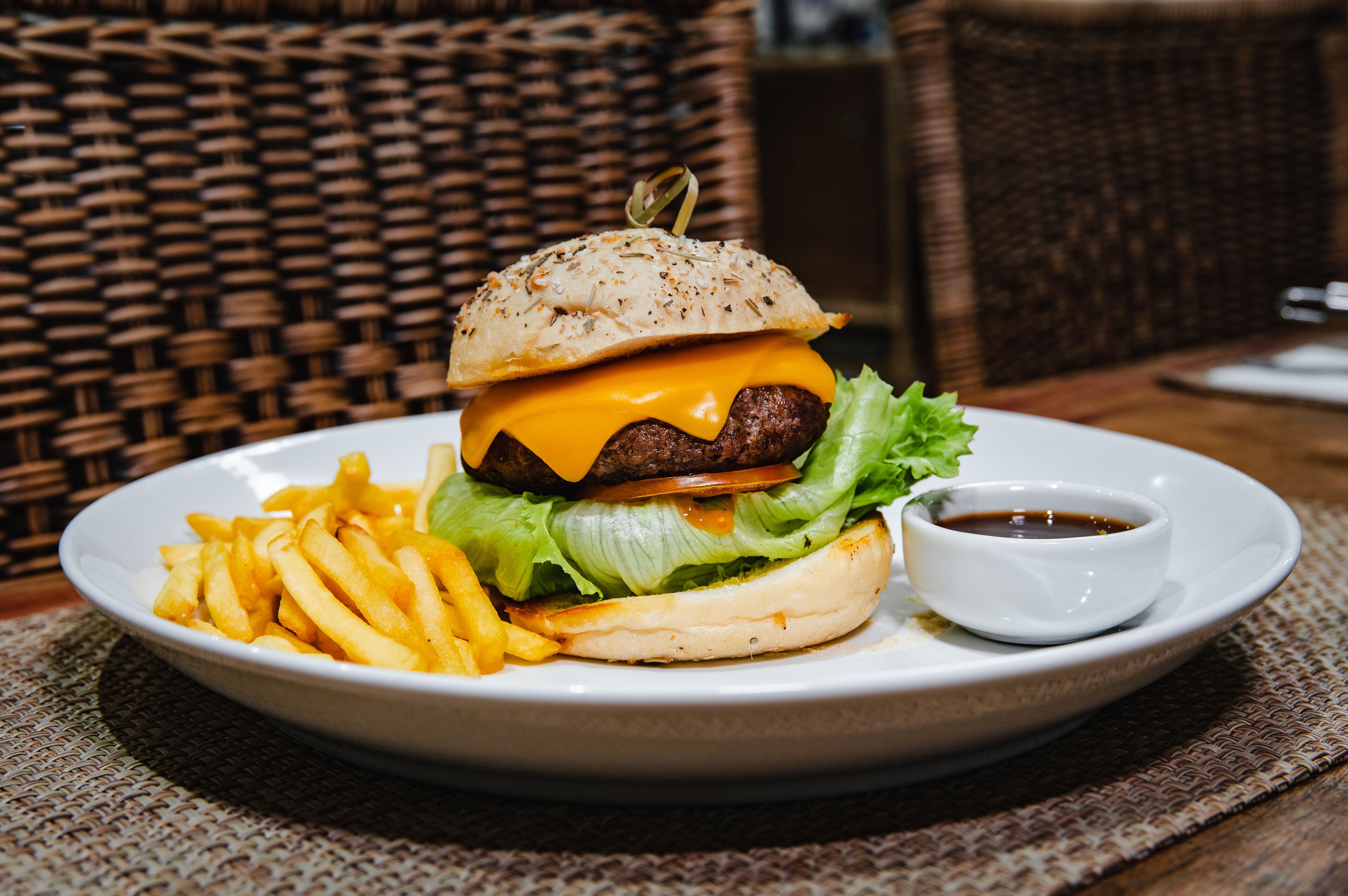 Un plato con una hamburguesa, papas fritas y una pequeña taza de salsa.