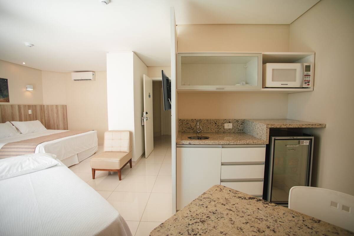A compact hotel room with a kitchenette, a bed, a chair, and a small table.