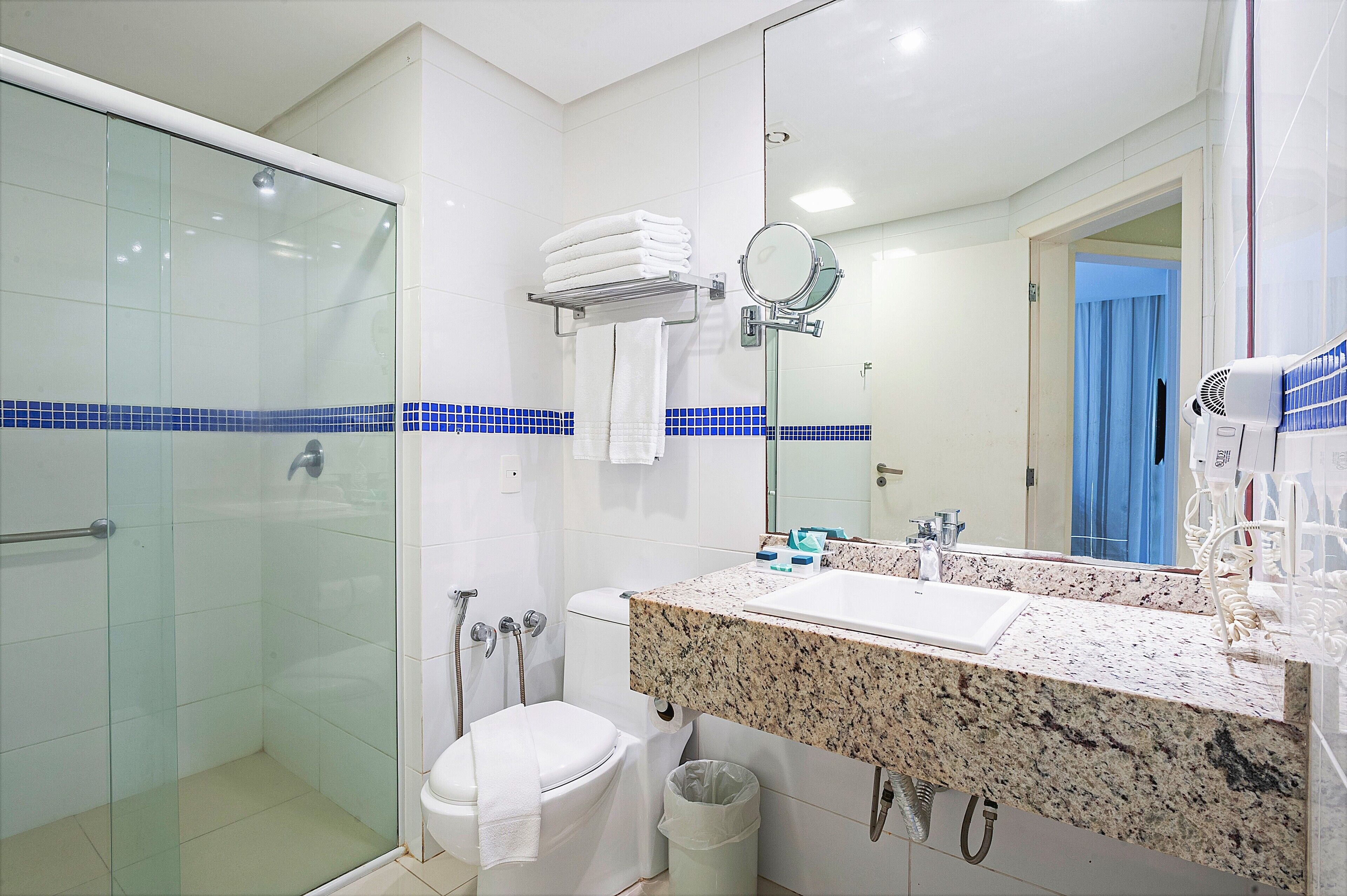 A bathroom with a glass shower enclosure, a toilet, a sink with a granite countertop, and a mirror.