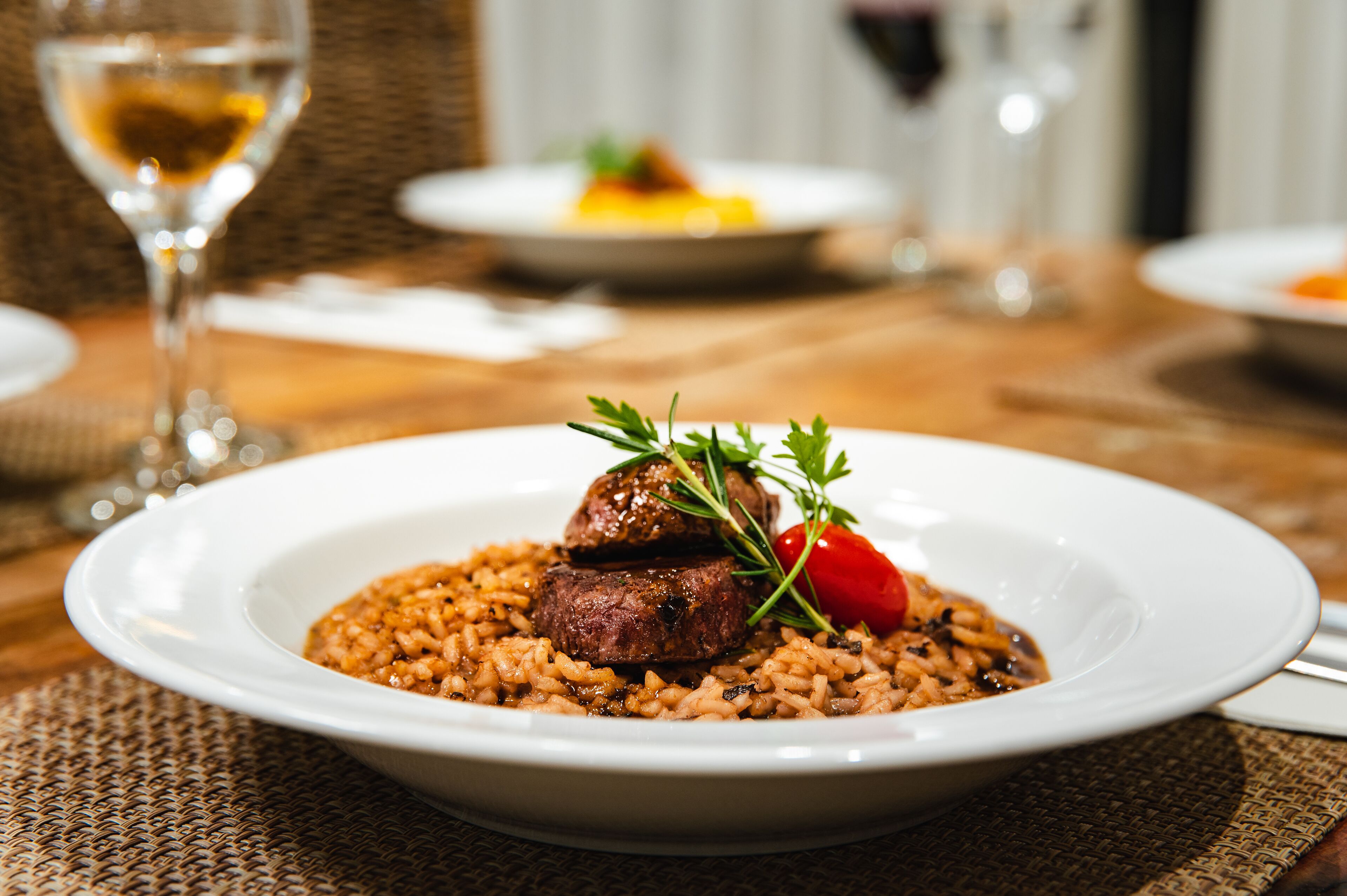 A plate of food with a steak and rice, garnished with a cherry tomato and parsley, on a table with a woven placemat.