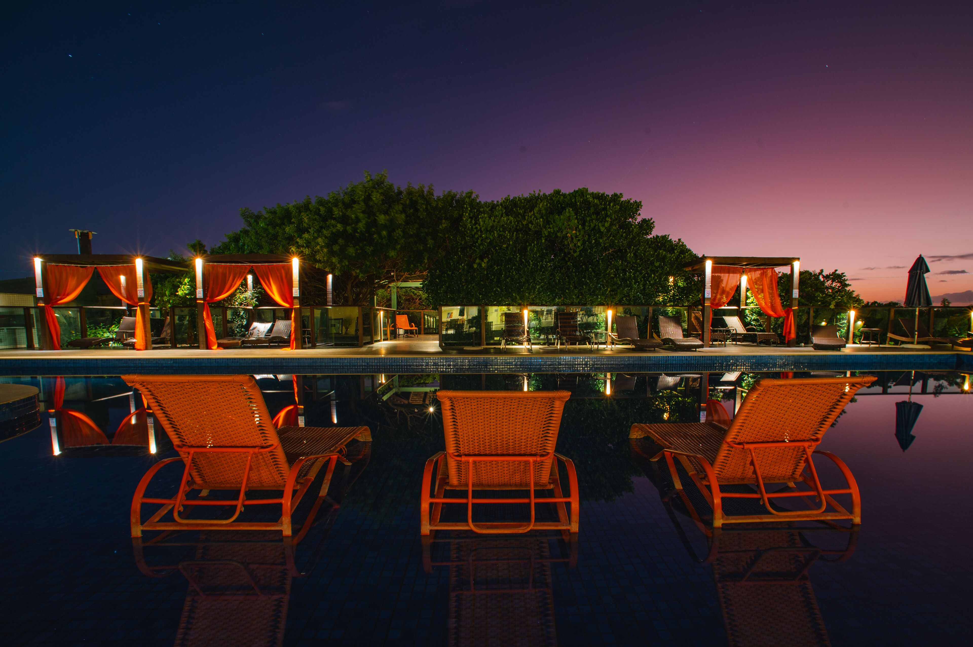 A pool area with lounge chairs and a covered seating area at dusk.