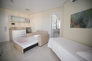 Habitación de hotel moderna con cama, sofá, kitchenette y baño visible a través de una puerta abierta.