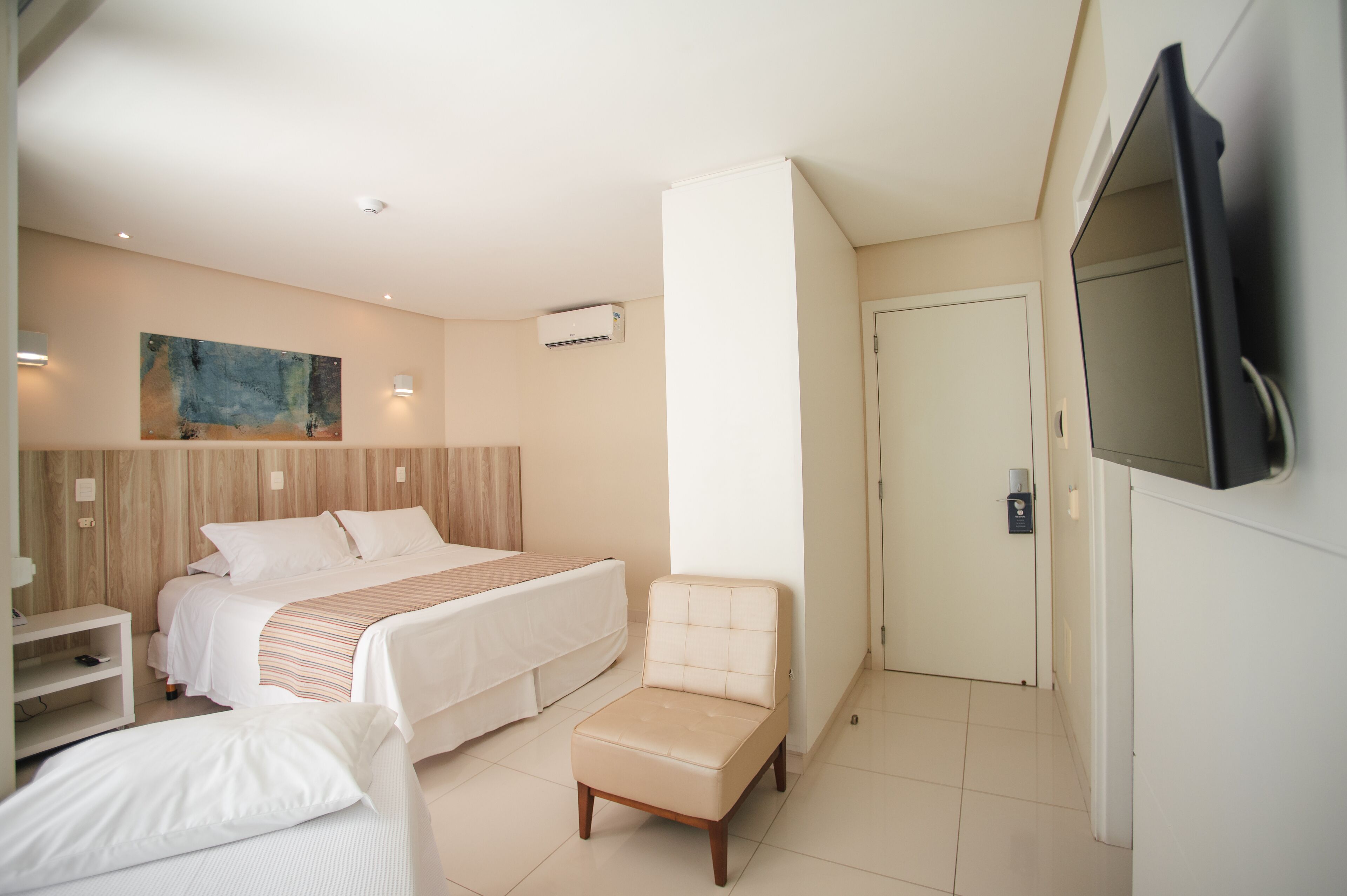 Una habitación de hotel con cama, una silla, un televisor y un cuadro en la pared.