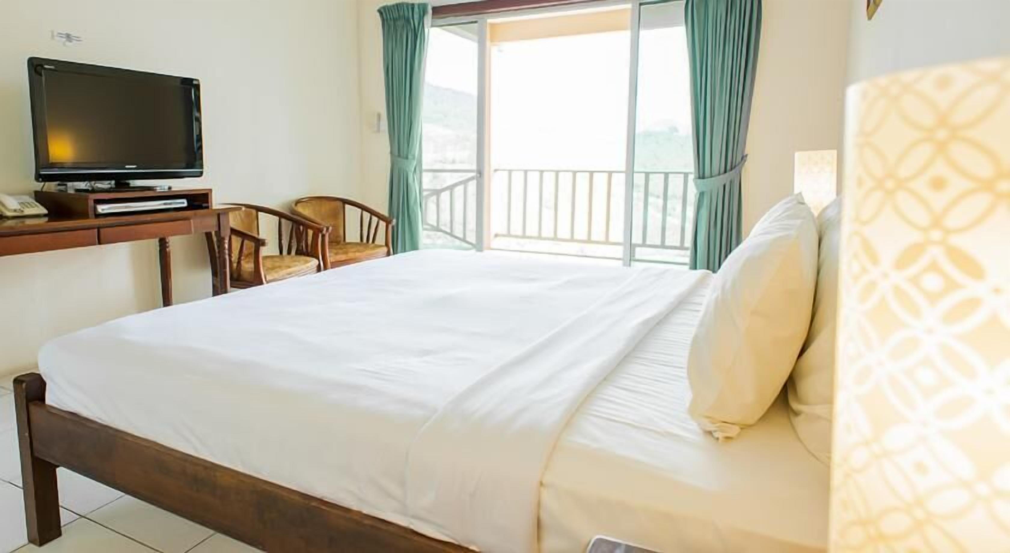 Une chambre d’hôtel avec un lit, une télévision, un bureau avec une chaise et un balcon avec des rideaux.