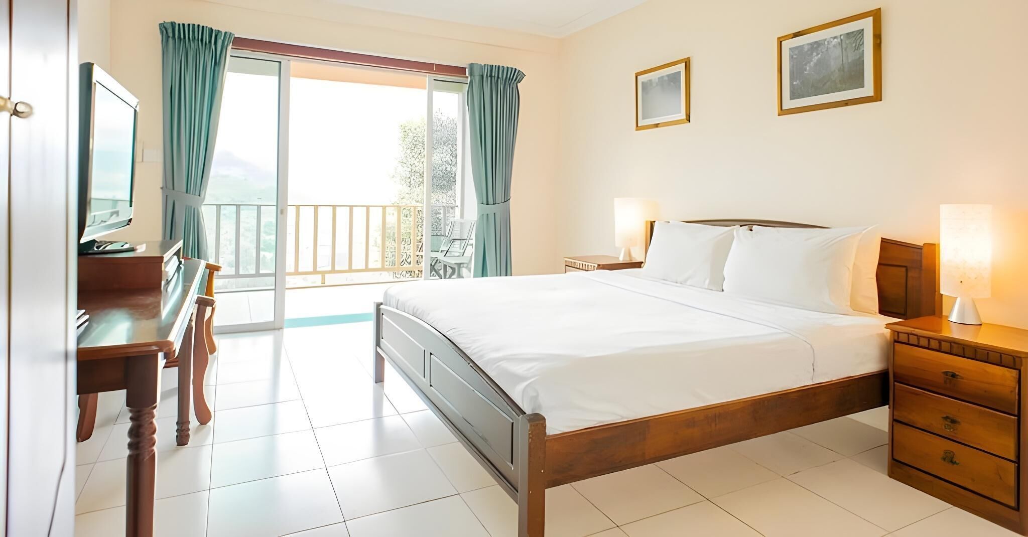 A hotel room with a bed, a desk, a chair, a nightstand, and a lamp.
