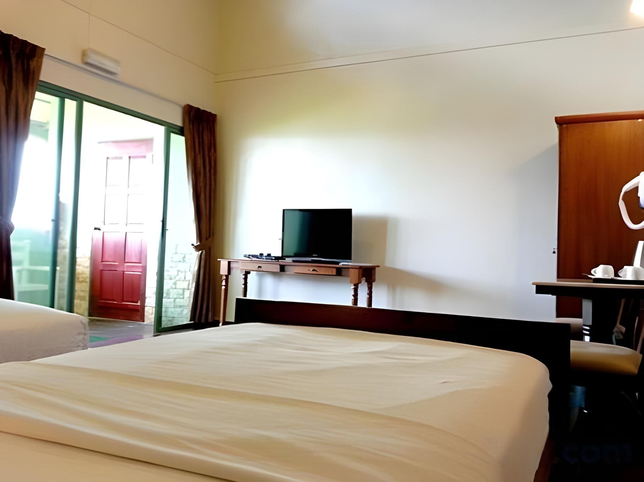 A hotel room with a bed, a television on a wooden stand, a desk with a chair, and a wardrobe.