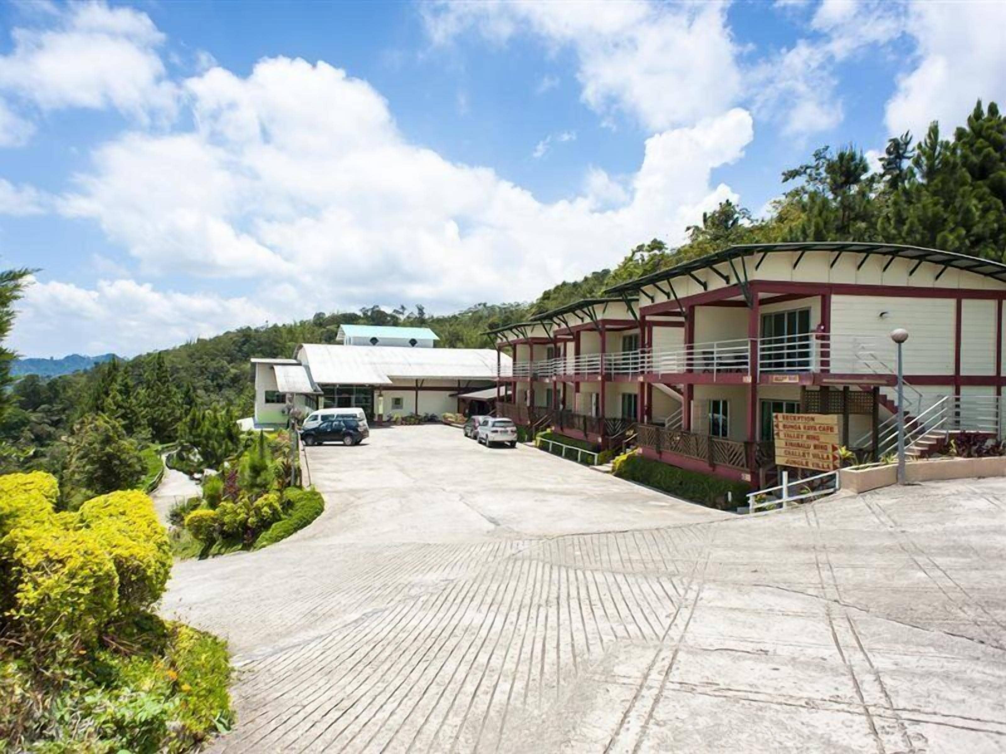 A hotel with a covered outdoor area, a parking lot, and a signboard listing amenities.