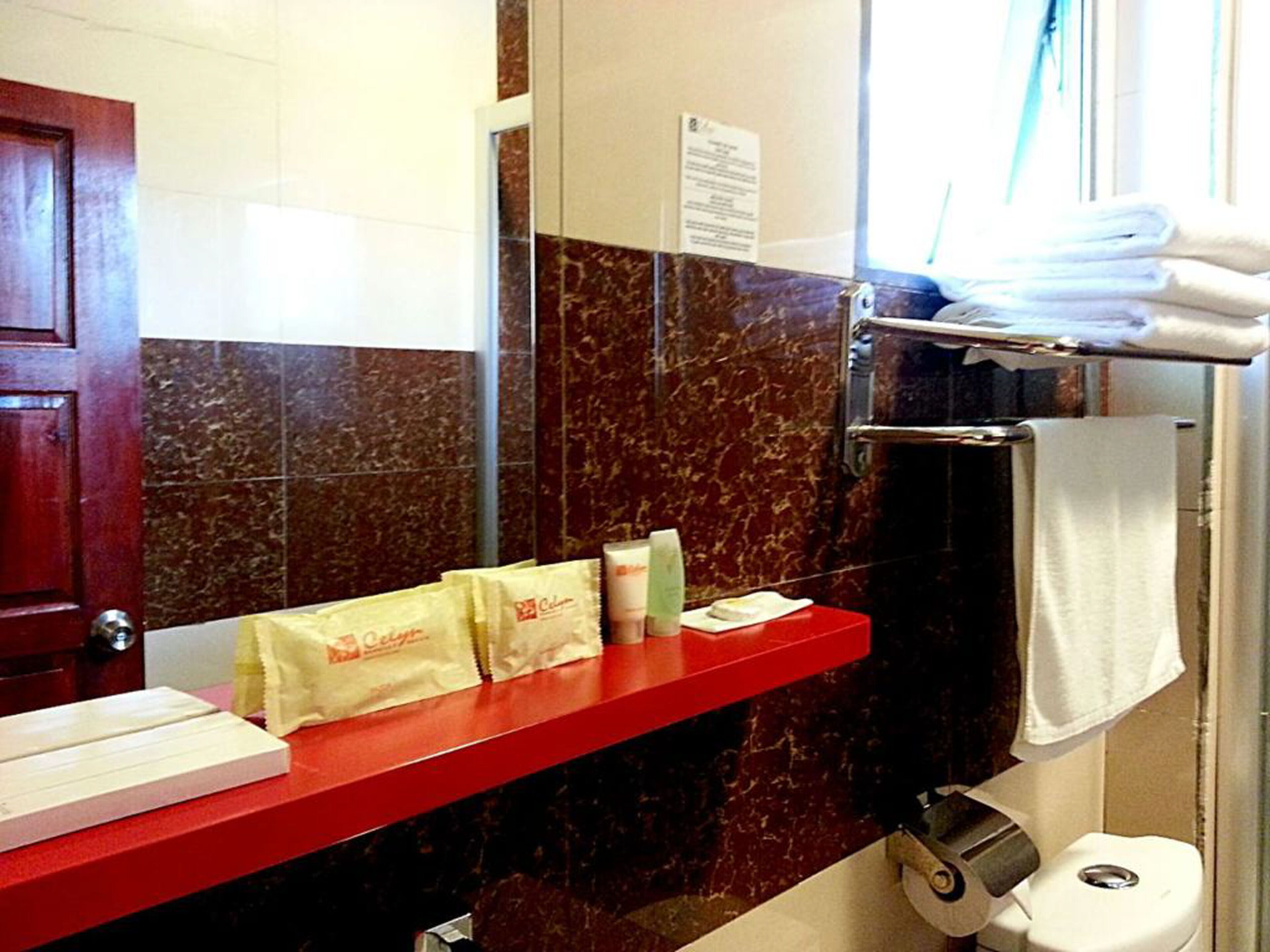 Une salle de bain avec un plan de toilette rouge, des murs en marbre, un porte-serviettes et des toilettes.