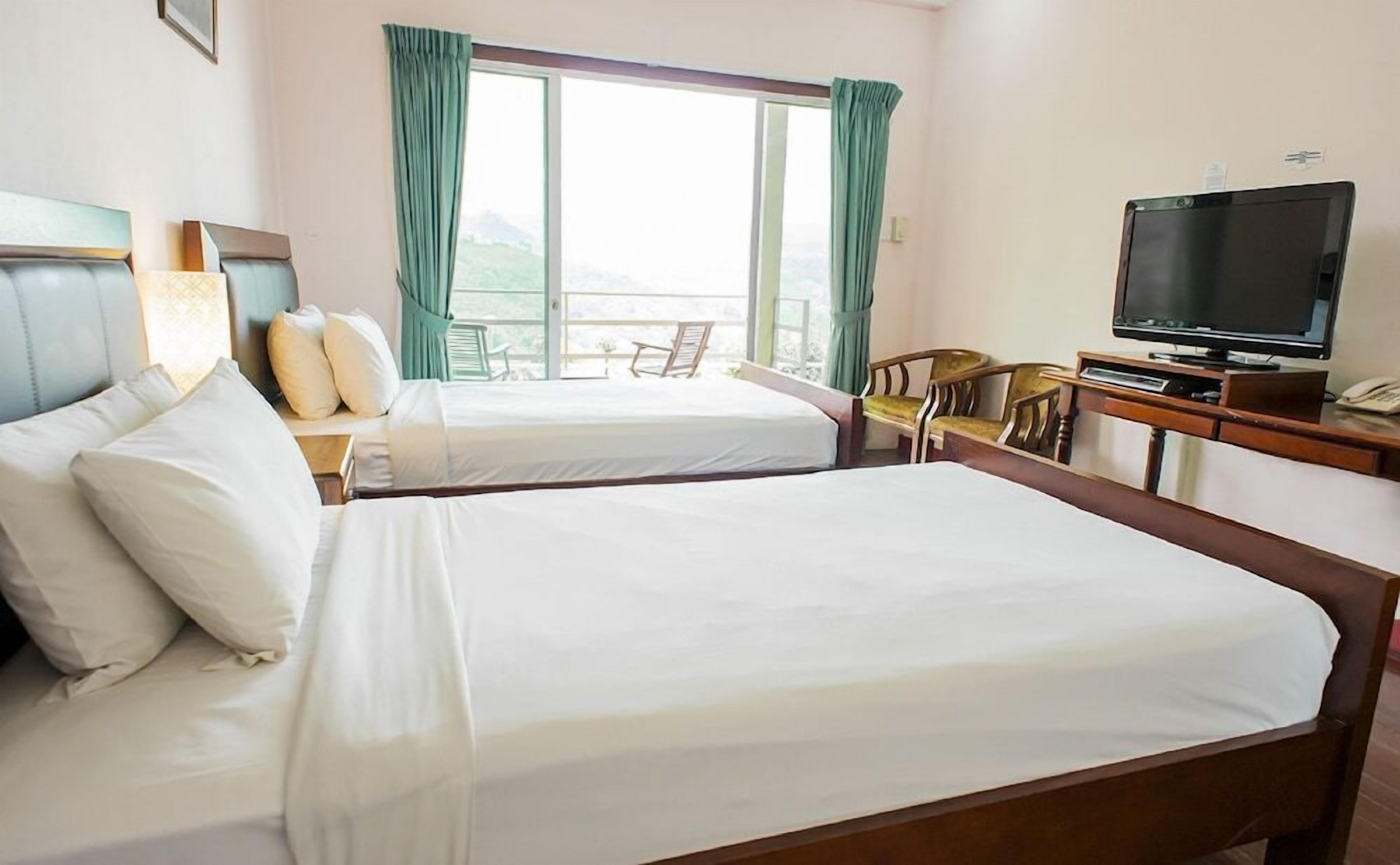 A hotel room with two beds, a TV, a desk, and a balcony with a view.