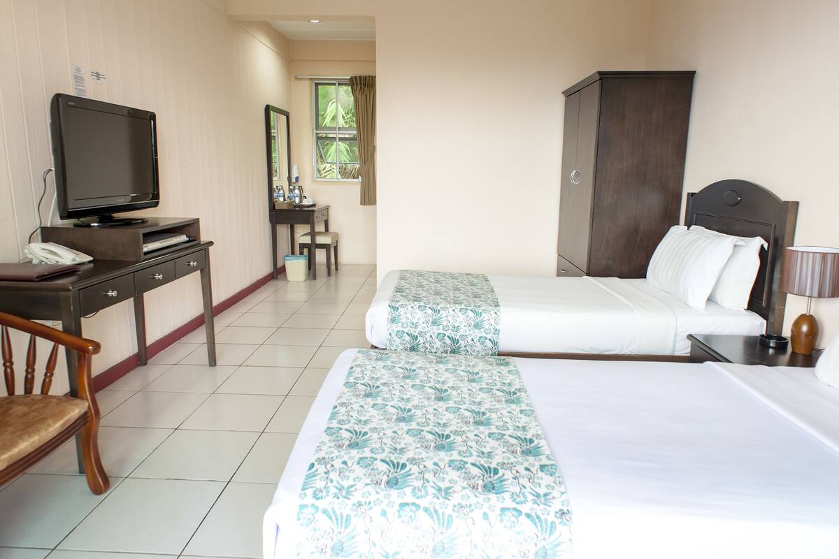 A hotel room with two beds, a desk with a television, a chair, and a wardrobe.