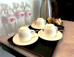 Una bandeja con cuatro tazas y platillos blancos, y tres botellas de agua.