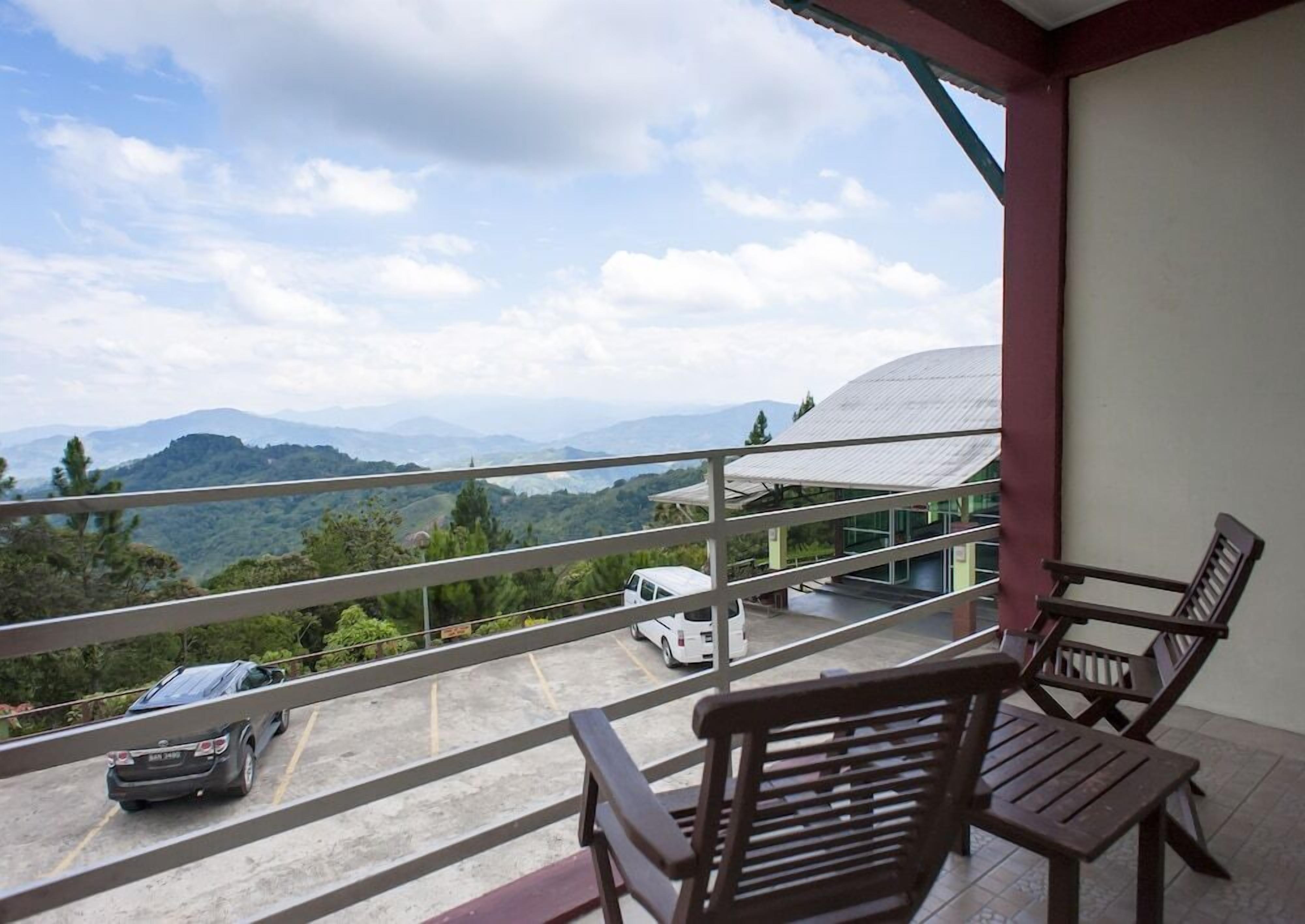 A balcony with a view of a mountainous landscape, a white car, and wooden furniture.