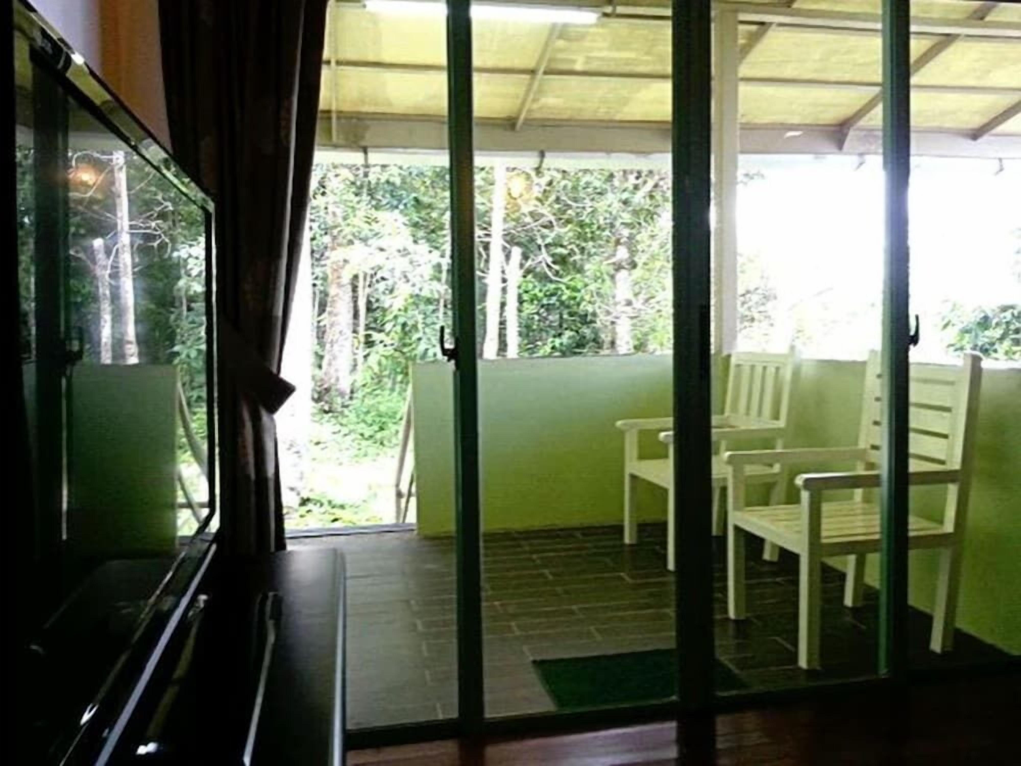 A room with a sliding glass door leading to an outdoor area with chairs and a view of greenery.