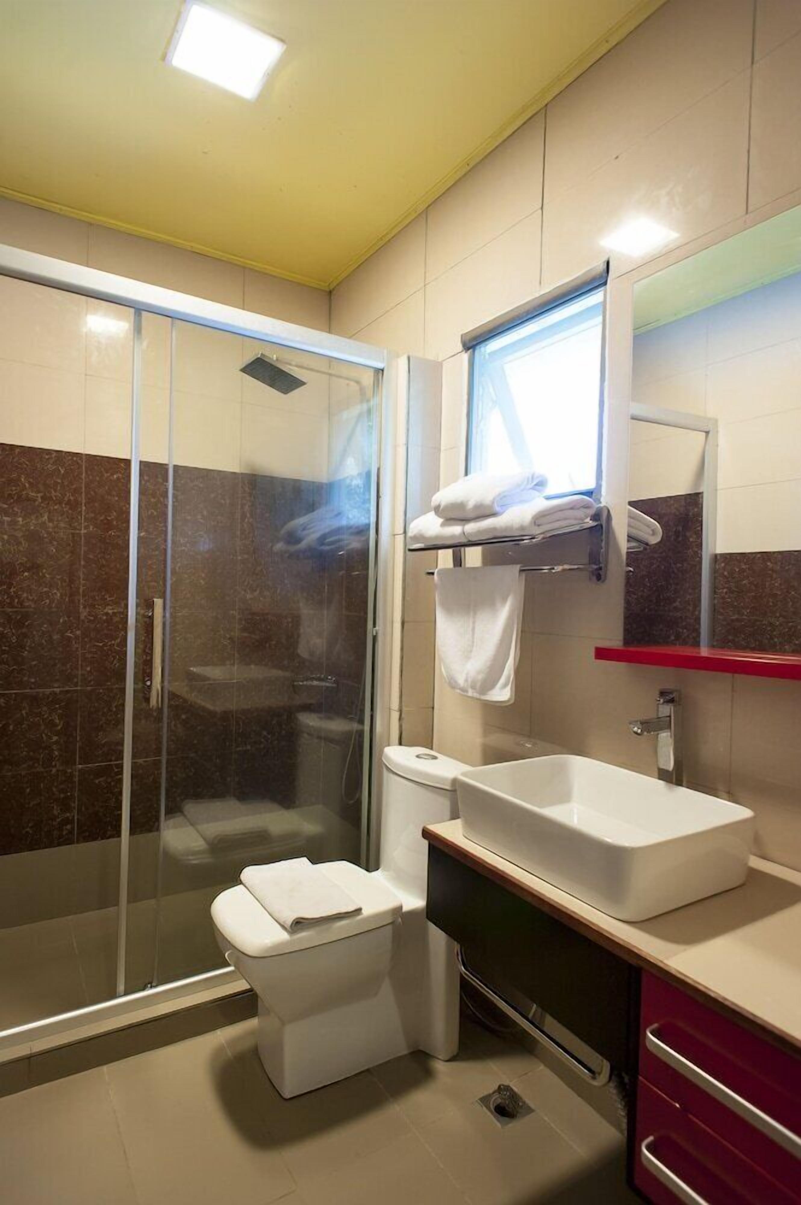 Un baño moderno con ducha acristalada, inodoro blanco, lavamanos y espejo.