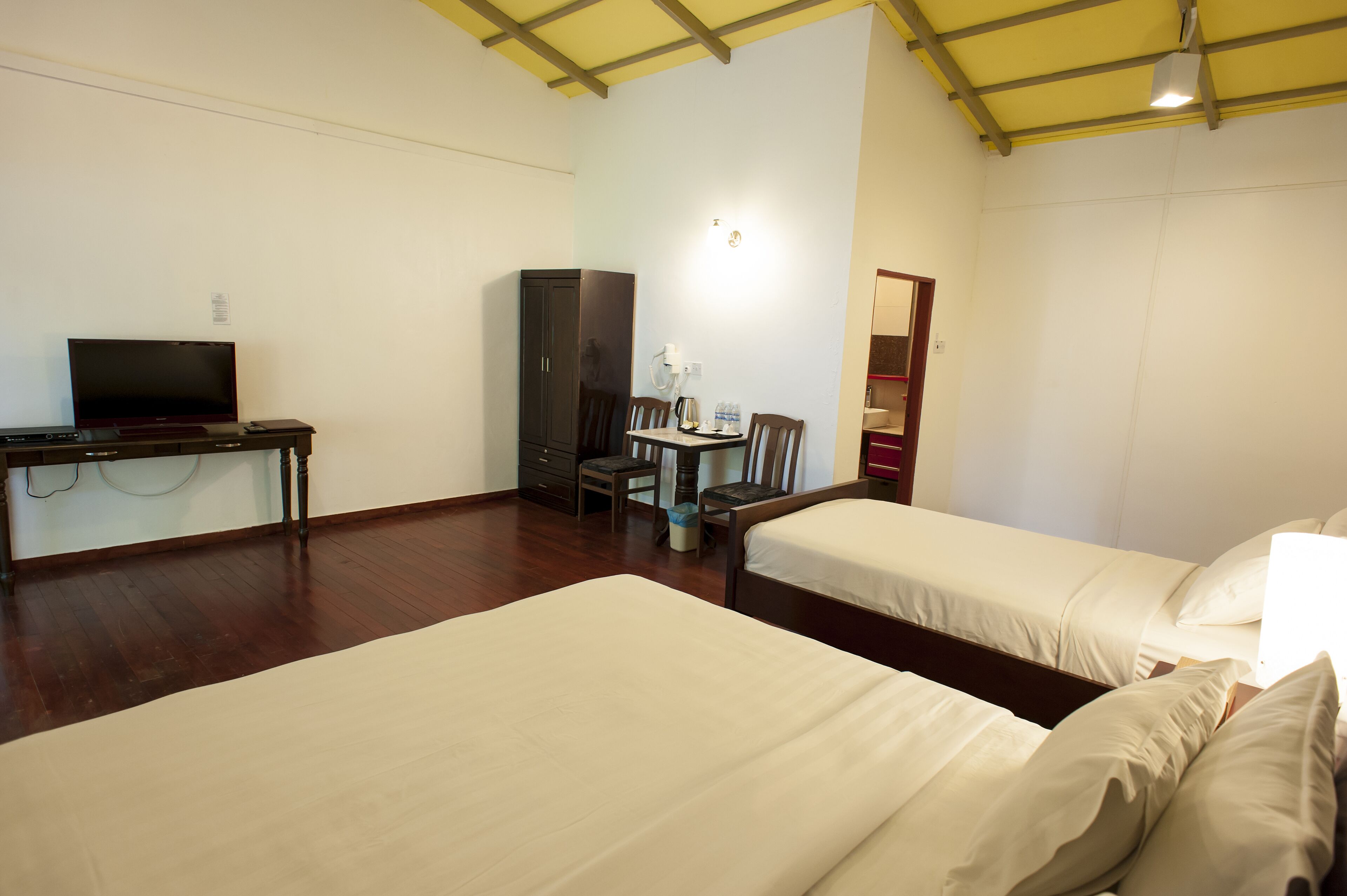 A hotel room with two beds, a desk with a television, a wardrobe, and a small table with chairs.