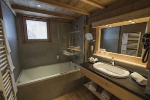 Un baño moderno con ducha de vidrio, bañera independiente, tocador con lavamanos y un espejo grande.
