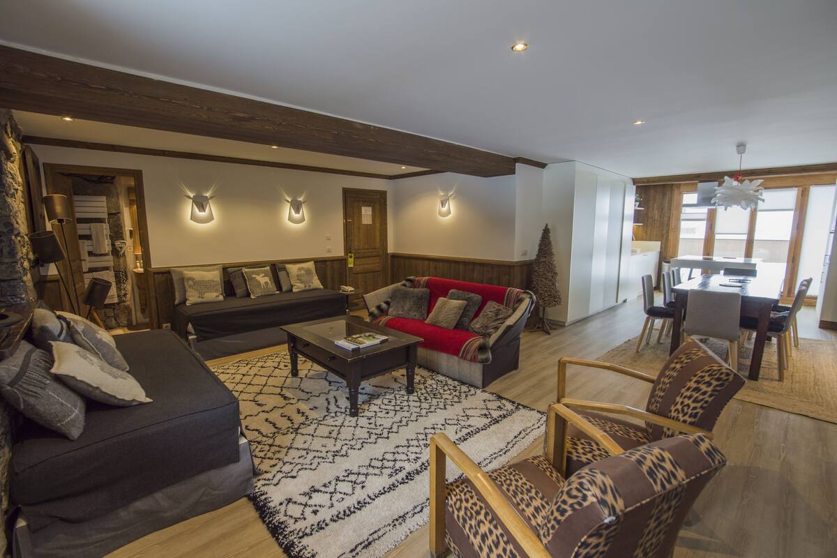 A modern living room with a sofa, armchairs, and a coffee table. There is a dining area with a table and chairs.