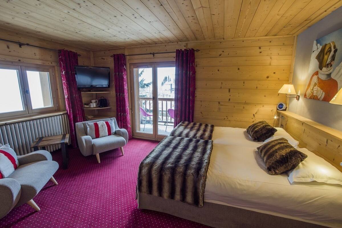 A cozy room with a bed, a sofa, a TV, and a window with curtains.