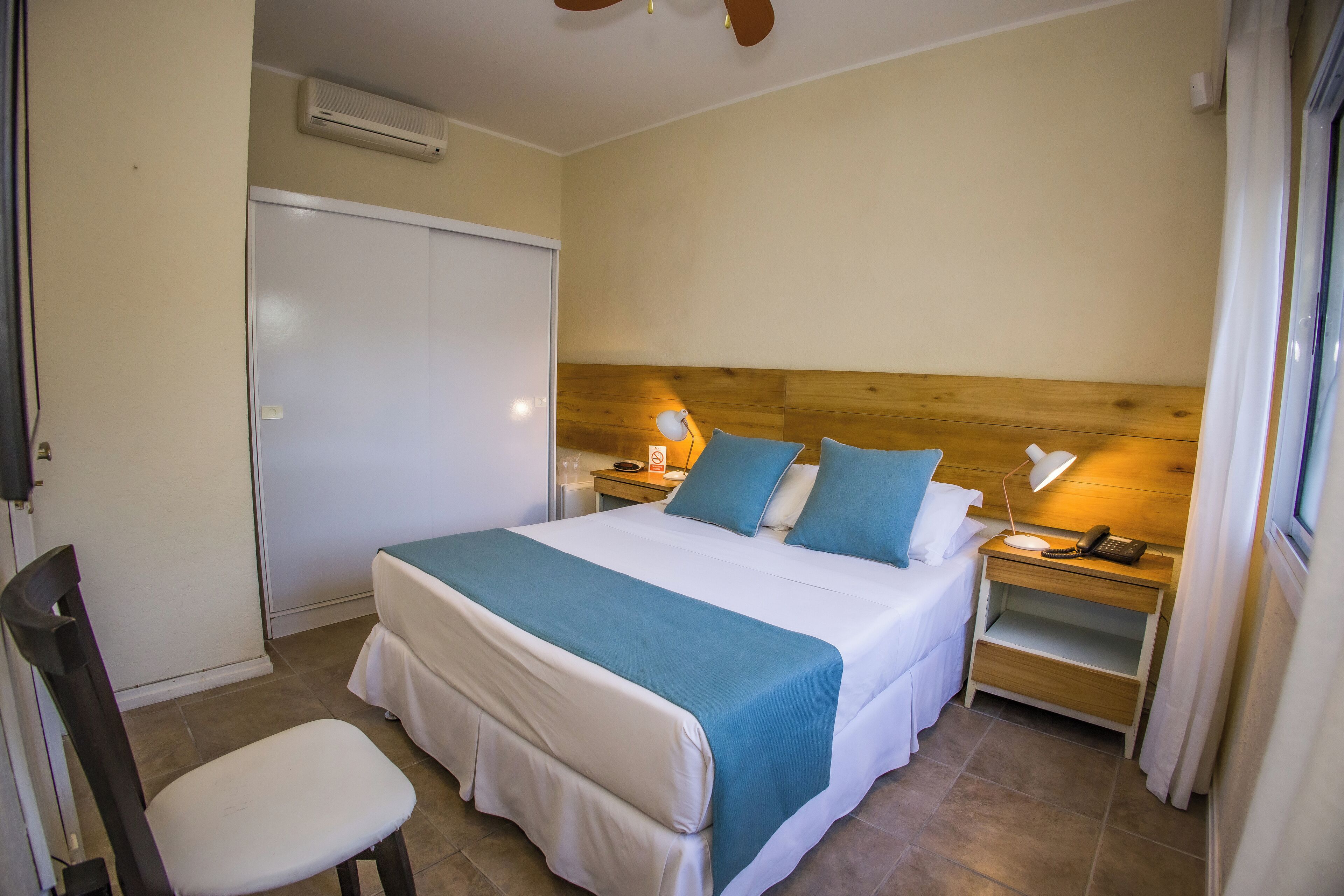 Una habitación de hotel con cama, mesitas de noche, una silla y un armario.