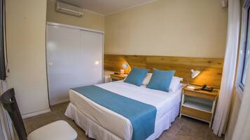 Una habitación de hotel con cama, mesitas de noche, una silla y un armario.