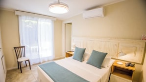 Hotellihuone, jossa on sänky, tuoli, yöpöytä ja ikkuna, jossa on verhot.