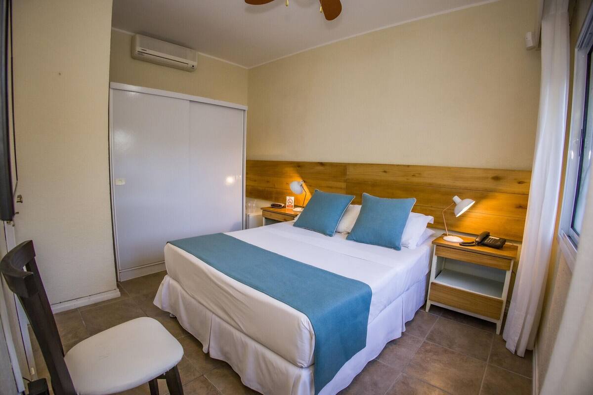 Habitación de hotel con cama, mesitas de noche, una silla, escritorio y aire acondicionado.