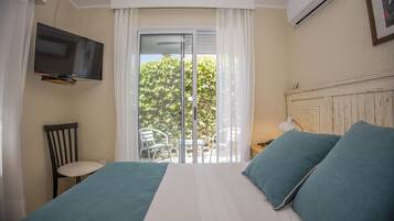 A bedroom with a bed, a TV mounted on the wall, a chair, and a view of the outdoors through a sliding door.