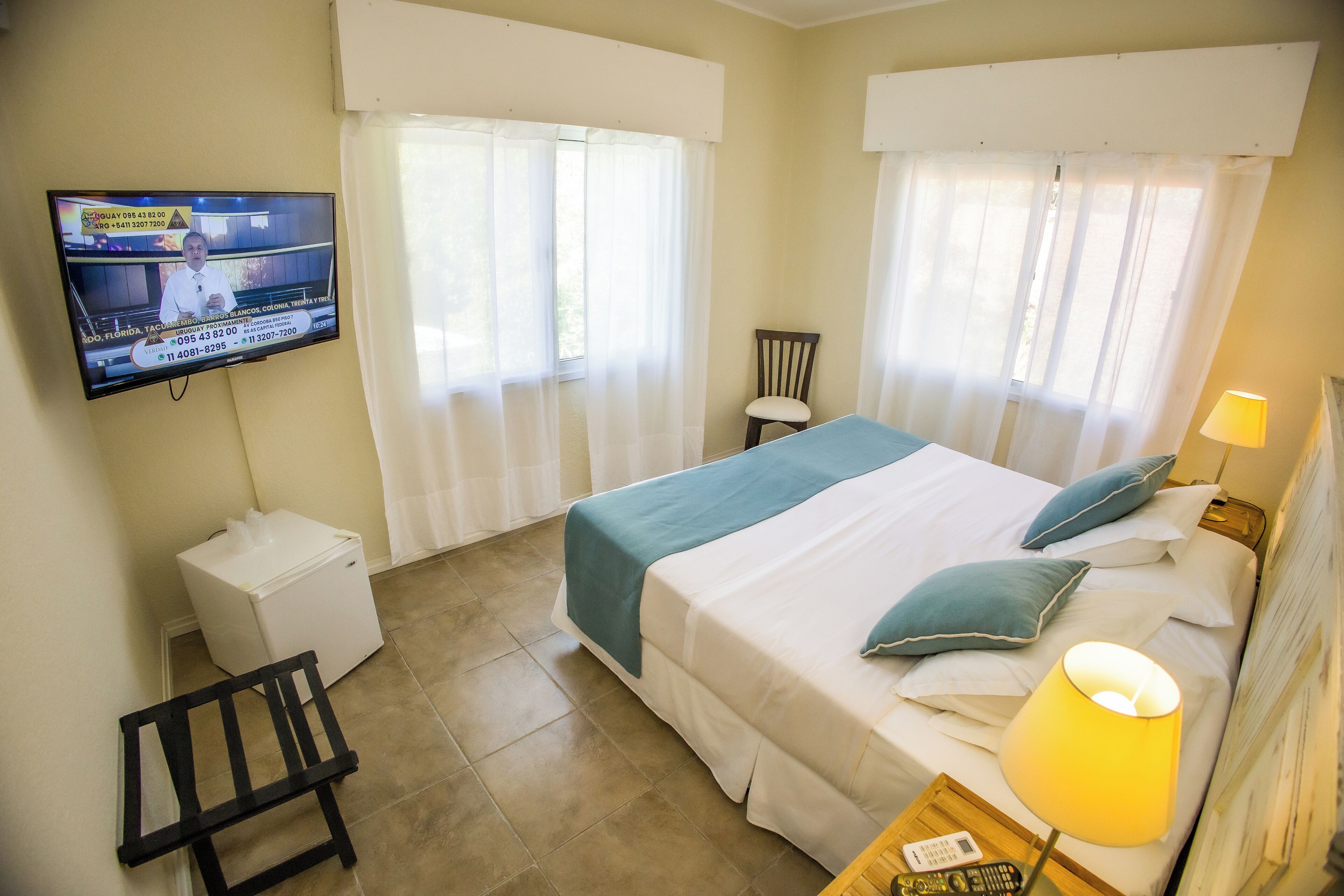 A hotel room with a bed, a desk, a chair, a television, and a window with curtains.