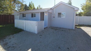 A single-story house with a covered porch, a fenced yard, and a gravel driveway. - Plovers Cove Cottage (Wasaga Beach)