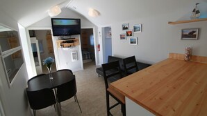 A compact kitchen with a wooden table and chairs, a TV mounted on the wall, and a small dining area. - Plovers Cove Cottage (Wasaga Beach)